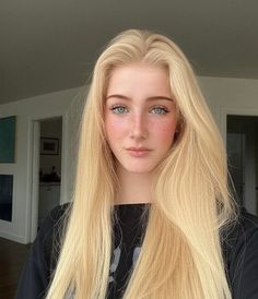 Young woman with long blonde hair and blue eyes, wearing a black shirt indoors