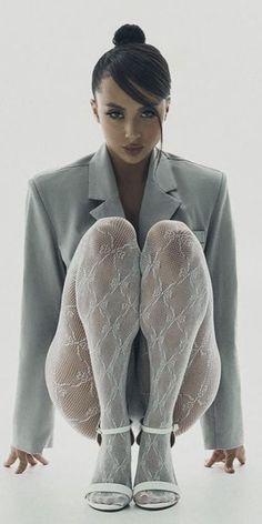 Woman in a gray blazer and white fishnet stockings squatting in a studio