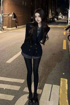 Woman with long dark hair wearing a blazer and shorts on a street at night