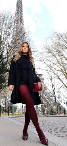 Woman in a black coat and red tights posing outdoors with the Eiffel Tower in the background