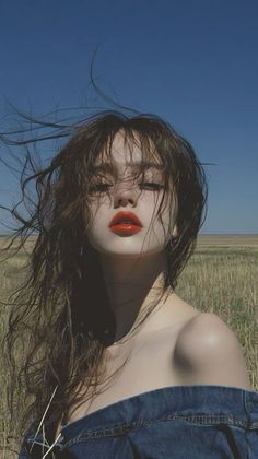 Woman with long, wind-blown hair and red lipstick in a field under a blue sky