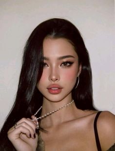 Woman with long black hair and a pearl necklace, looking at the camera