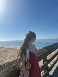 Woman in a red dress with a ponytail looking out at the ocean from a pier