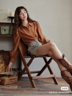 Woman with long hair wearing a brown shirt, shorts, and cowboy boots, sitting indoors