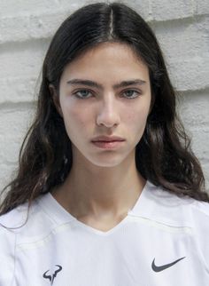 Woman with long dark hair wearing a white v-neck shirt against a white background