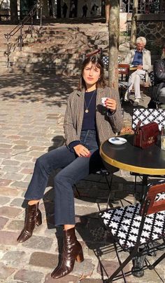 Woman in a plaid blazer and brown boots sitting at an outdoor cafe