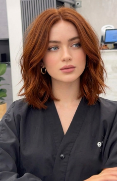 Woman with red, wavy short hair and blue eyes wearing a black top indoors