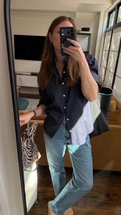 Woman in a black shirt and blue jeans taking a mirror selfie indoors