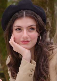 Woman with long wavy hair and a black beret, resting her chin on her hand