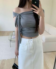 Woman in an off-shoulder crop top and white skirt taking a mirror selfie