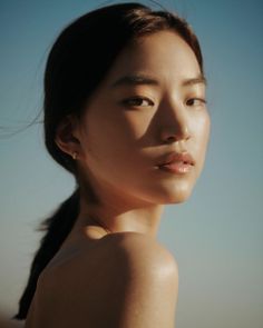 Woman with dark hair in a ponytail, bare shoulders, in soft outdoor lighting