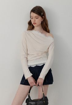 Woman with long hair wearing an off-shoulder top and mini skirt, holding a black handbag