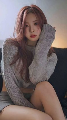 Woman with long hair in a grey sweater and shorts, sitting indoors