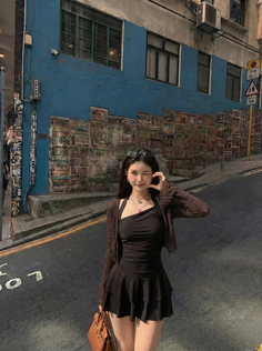 Woman in a black dress and brown cardigan posing on a street