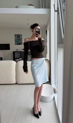 Woman in an off-shoulder top and light blue skirt taking a mirror selfie indoors