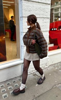 Woman in a fair isle cardigan, mini skirt, and tights walking on a street