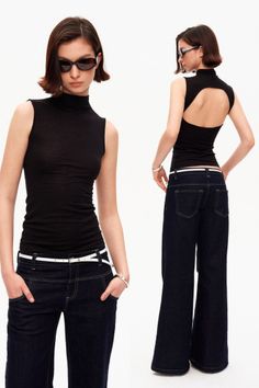 Woman in a black top and dark jeans with a white belt, posing in a studio