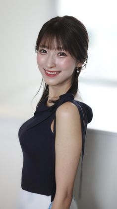Woman with dark hair and pearl earrings smiling in a sleeveless top