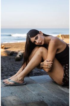Woman with long dark hair sitting on a stone ledge at the beach