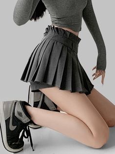 Person in a gray crop top and pleated skirt kneeling in a studio