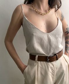 Person wearing a gold chain necklace, sleeveless top, and light colored pants