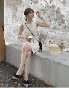 Woman in a sleeveless dress sitting on a concrete bench with a coffee cup