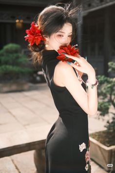 Woman in a black cheongsam with red flowers in her hair and holding a flower