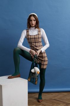Woman in a plaid dress and green tights holding a mesh bag with a duck toy