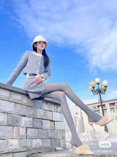Woman in a gray skirt suit and bucket hat sitting outdoors under a blue sky