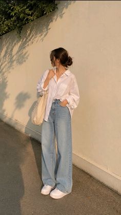 Woman in a white shirt and wide leg jeans standing outdoors at golden hour