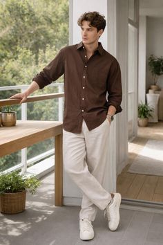 Man in a brown shirt and white pants standing on a balcony