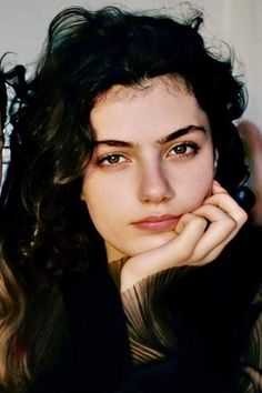 Woman with dark, curly hair resting her chin on her hand