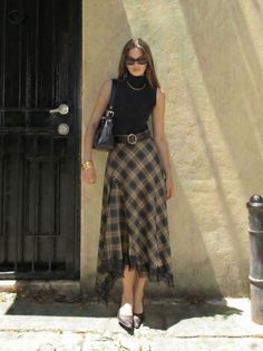 Woman in a black top and plaid skirt with sunglasses standing outdoors