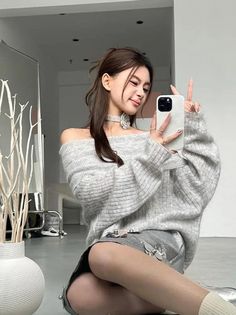 Woman in an off-shoulder sweater and silver shorts taking a selfie