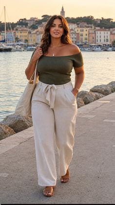 Woman in an off-shoulder top and wide-leg pants walking along a harbor at golden hour