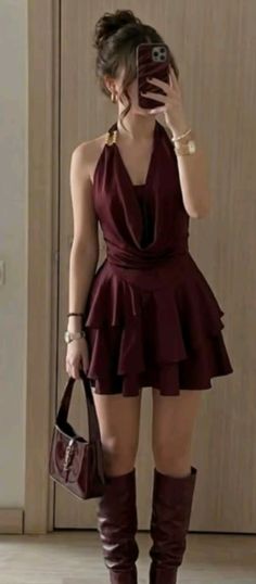 Woman in a burgundy halter dress and knee-high boots holding a handbag