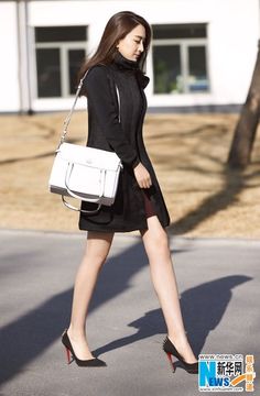 Woman in a black dress and high heels walking outdoors with a white handbag