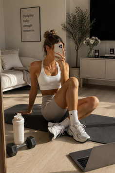 Woman in athletic wear taking a mirror selfie on a yoga mat indoors