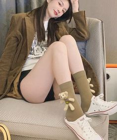 Woman with long hair wearing a brown jacket and teddy bear socks, sitting indoors