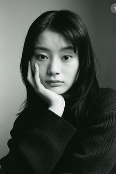 Woman with long black hair in a black sweater, resting her chin on her hand