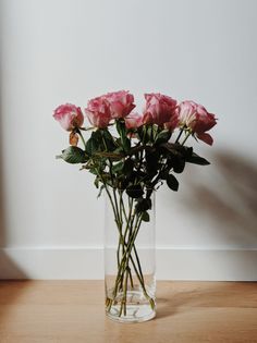 Pink roses in a glass vase against a white wall and wooden floor
