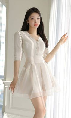 Woman in a white dress with a pleated skirt standing indoors