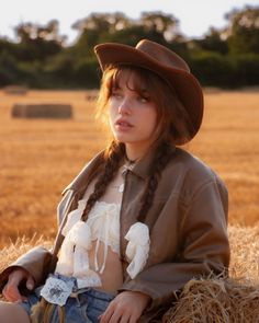 Woman in a cowboy hat and braids sitting on hay bales at golden hour