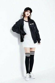 Woman in a black bomber jacket, white dress, and knee high socks posing in a studio