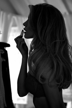 Woman applying lipstick in a backlit, black and white indoor shot