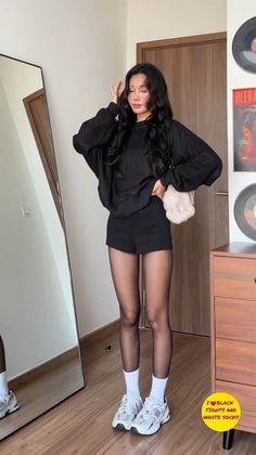 Woman in a black top, shorts, and tights posing in front of a mirror
