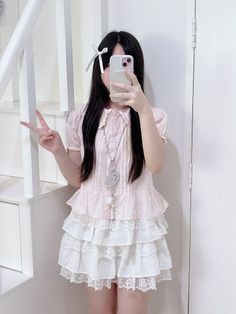 Person with long black hair in a pink top and ruffled skirt taking a mirror selfie