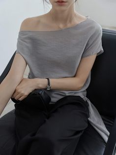 Woman in an off-shoulder top and black pants, sitting indoors