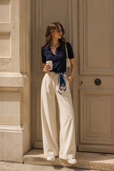 Woman in a navy polo shirt and wide leg pants holding a coffee cup outdoors