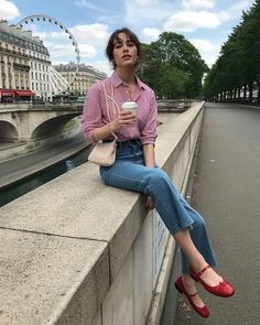 Woman in a striped shirt and jeans sitting on a stone wall with a city background